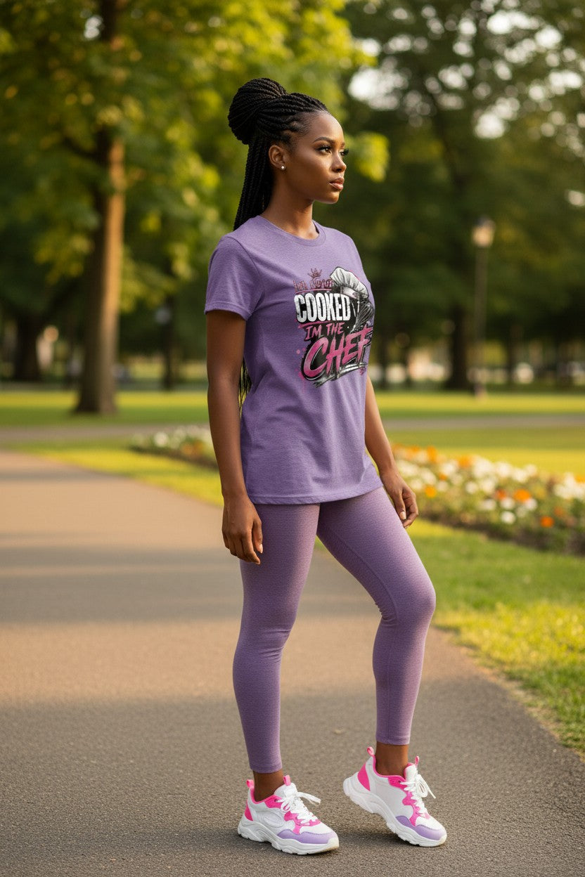 A woman stands on a paved path in a park wearing a matching lavender athletic set consisting of a short-sleeve graphic T-shirt and leggings, paired with pink and white sneakers.