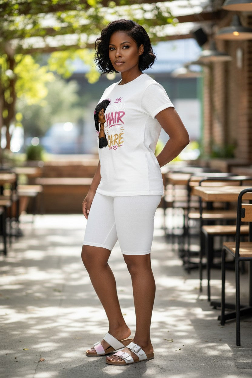 A woman modeling a white graphic t-shirt and matching white biker shorts in an outdoor patio setting with tables and trees in the background.