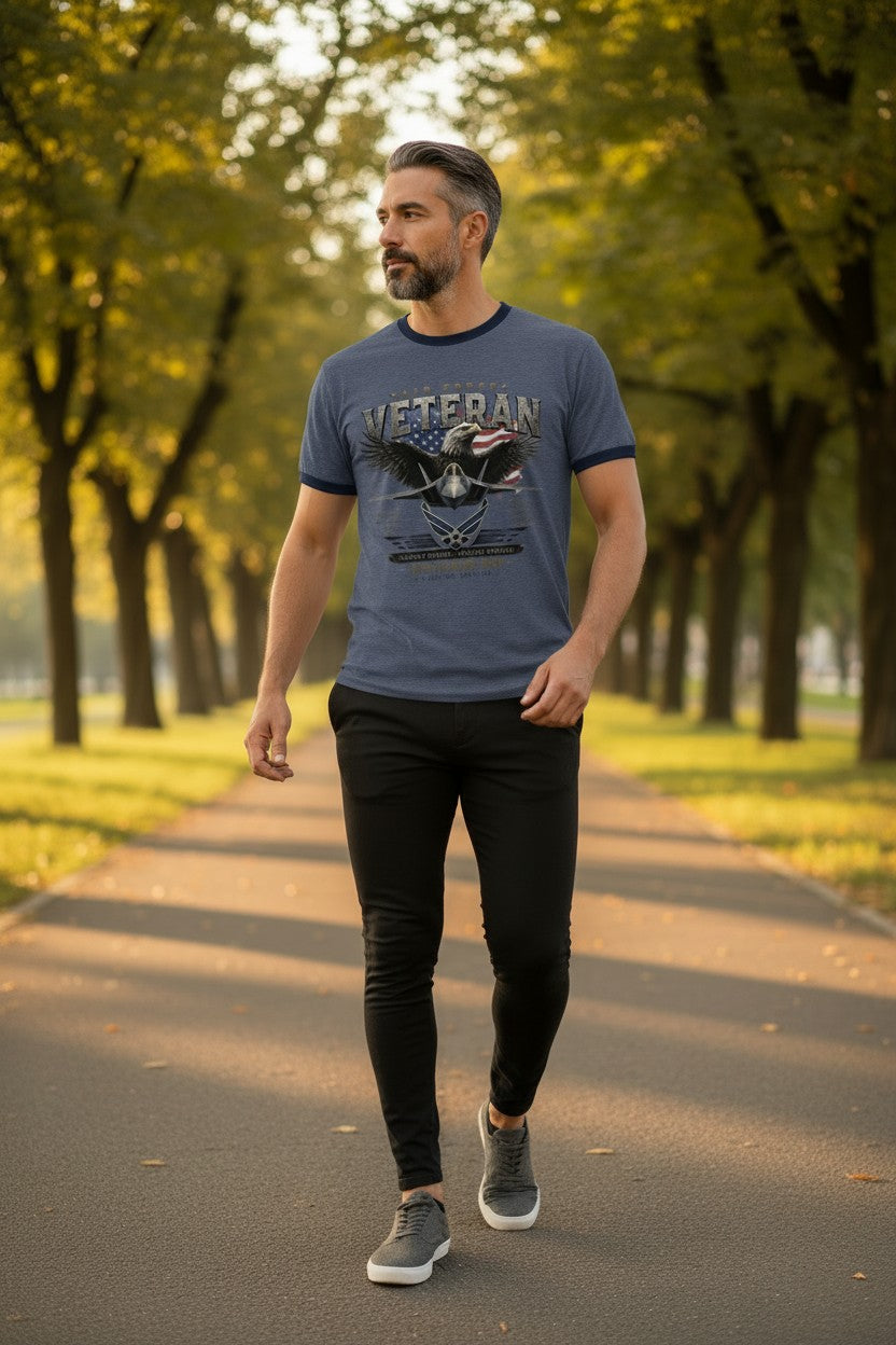 A man walking on a tree-lined path wearing a slate blue ringer t-shirt with a distressed graphic that reads 'VETERAN' and '20TH CENTURY FIGHTERS'.