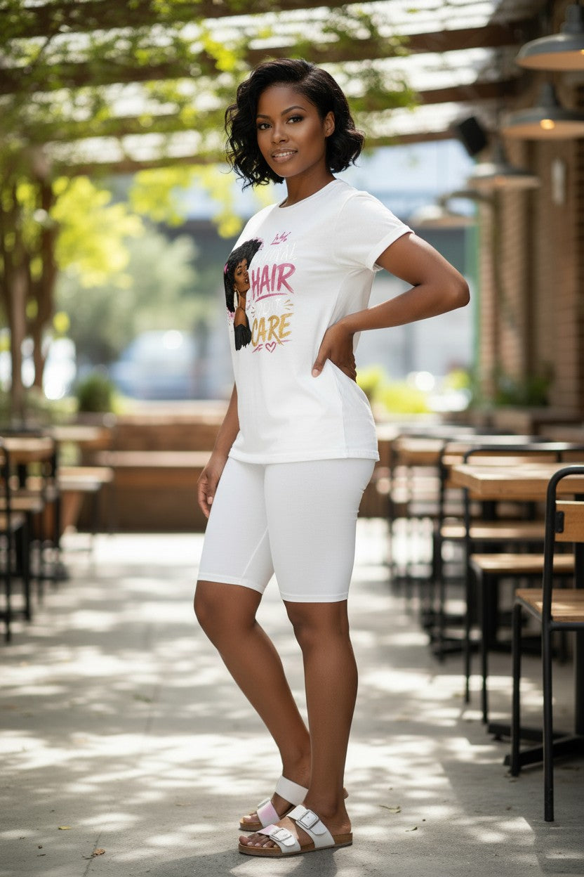 A woman modeling a white short-sleeve graphic T-shirt and matching white biker shorts in an outdoor patio setting with tables and greenery in the background.