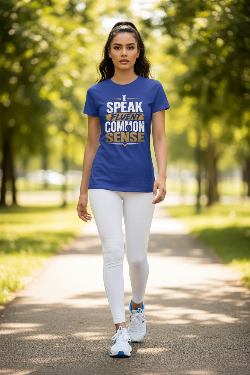A woman walking on a tree-lined path wearing a royal blue graphic t-shirt with the text 'I SPEAK FOR COMMON SENSE' in white and gold, paired with white leggings and white sneakers.