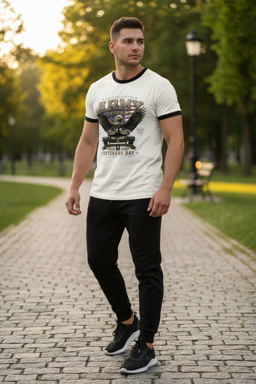 A man walking on a cobblestone path in a park, wearing a white ringer t-shirt with black trim and a graphic print, paired with black pants and black sneakers.