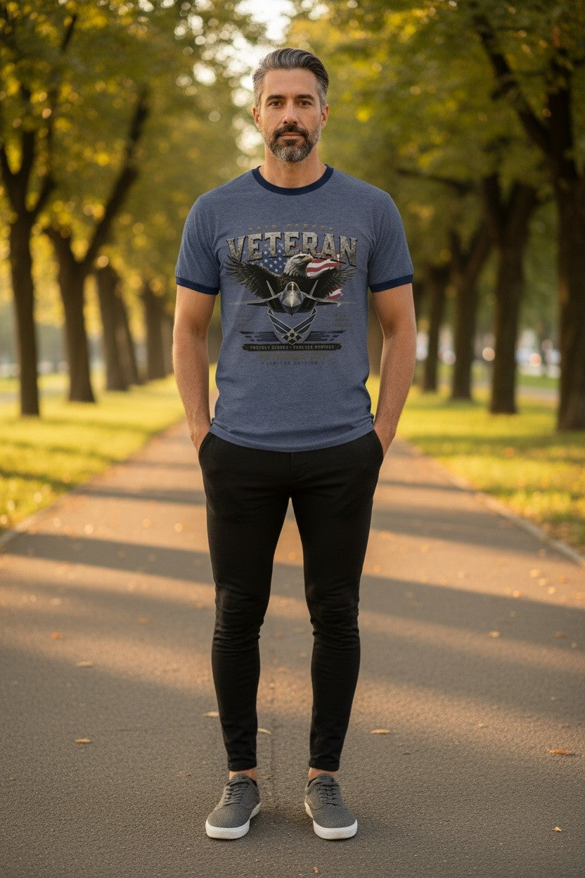 A man standing on a tree-lined path wearing a blue ringer t-shirt with a 'VETERAN' eagle graphic, black pants, and gray sneakers.