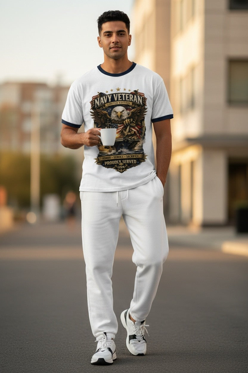 A man walking outdoors wearing a white ringer T-shirt with a large navy graphic print that reads 'NAVY VETERAN' and matching white sweatpants, holding a white mug.