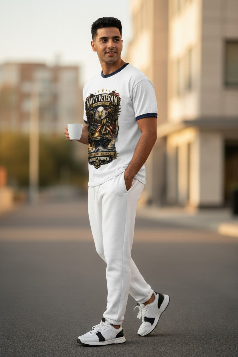 A man wearing a white ringer t-shirt with a dark graphic print and matching white sweatpants, walking outdoors on a city street while holding a white coffee mug.