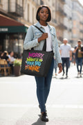 A woman walking on a city street carrying a black tote bag with colorful text that reads 'WORRY. WHAT'S IN YOUR BAG IS MY NINE.