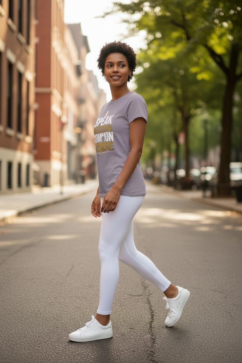 A woman walking on a city street wearing a light purple graphic t-shirt, white leggings, and white sneakers.