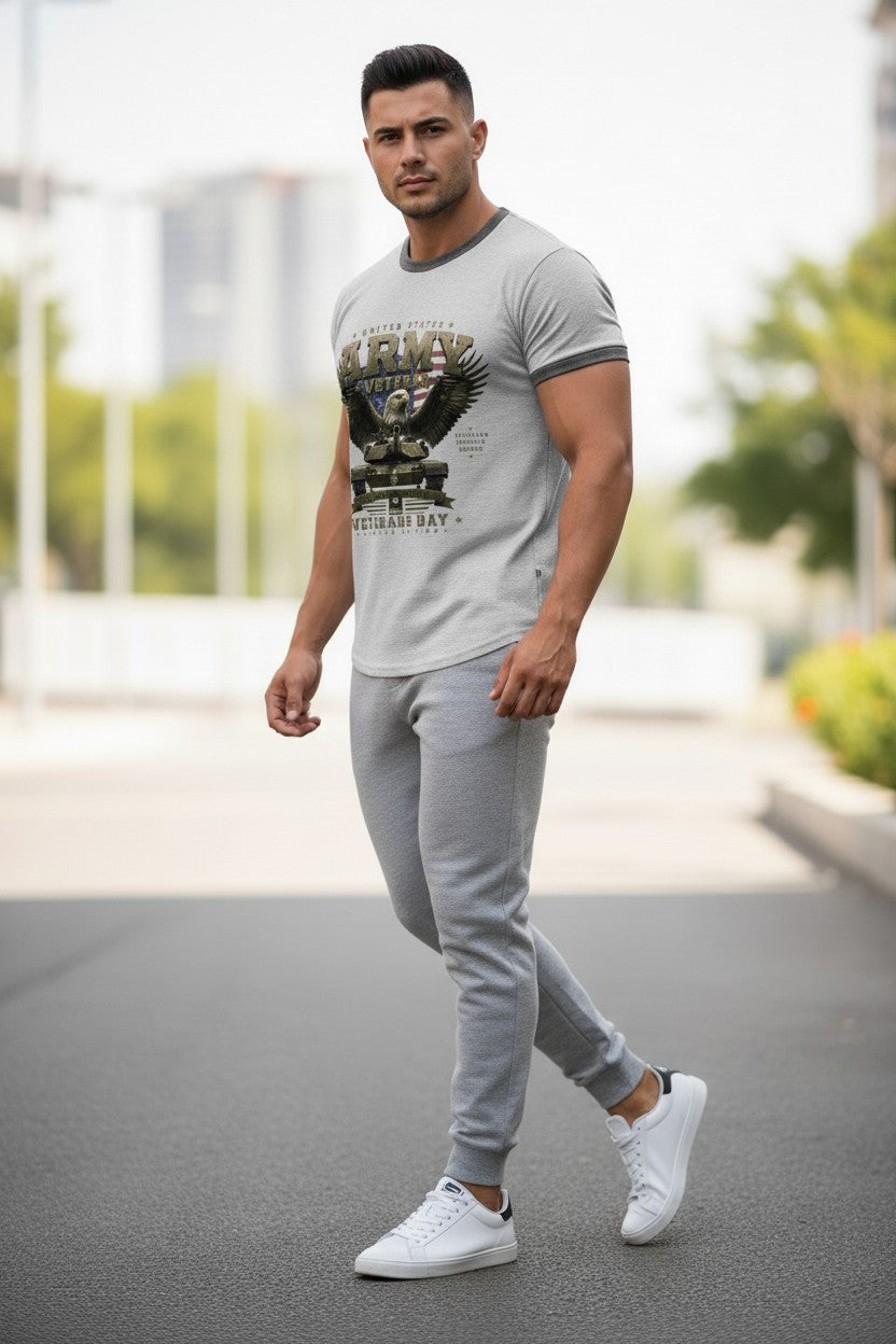 A man walking outdoors wearing a light gray ringer t-shirt with a graphic print, matching gray jogger pants, and white sneakers.