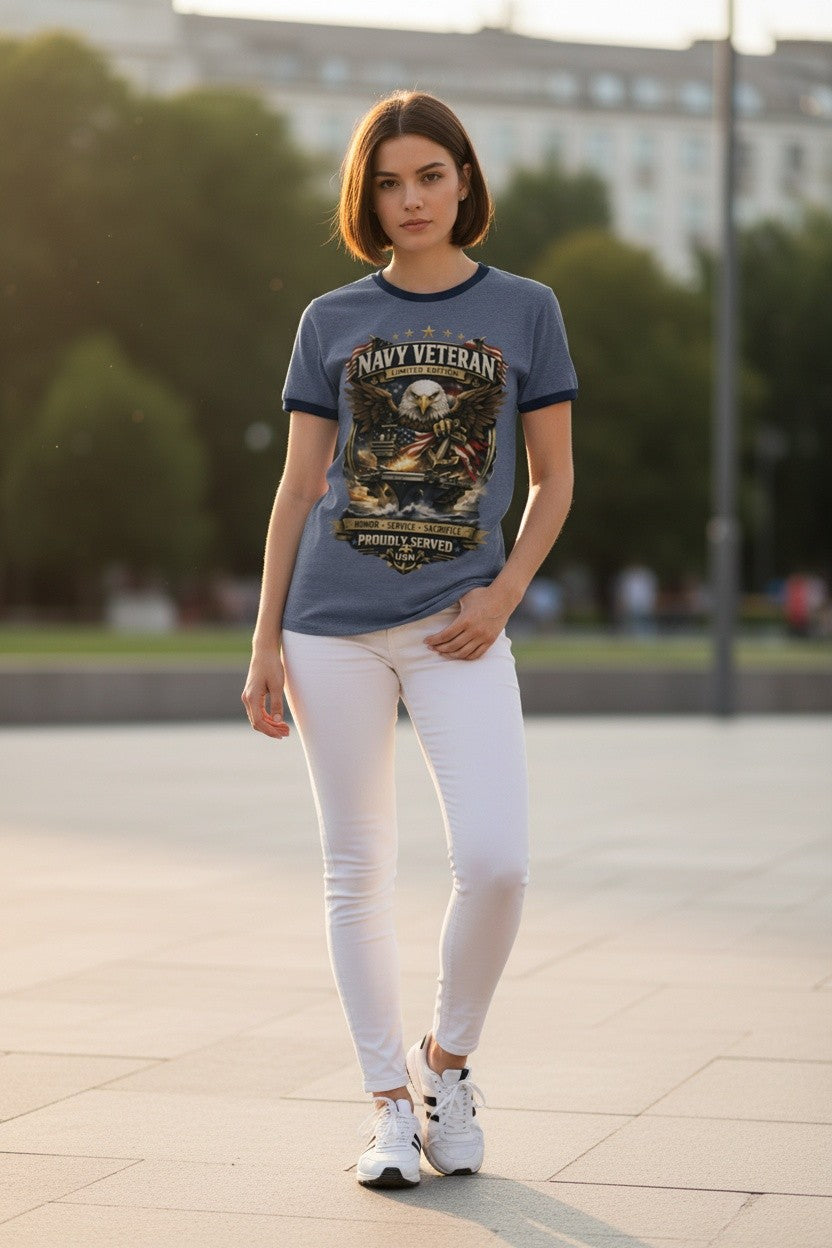 A woman wearing a slate blue graphic t-shirt with 'NAVY VETERAN' printed on the front, paired with white pants and white sneakers, standing outdoors on a paved walkway.
