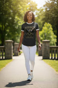 A woman walking on a sunny park path wearing a black graphic t-shirt with white trim, white leggings, and white sneakers.