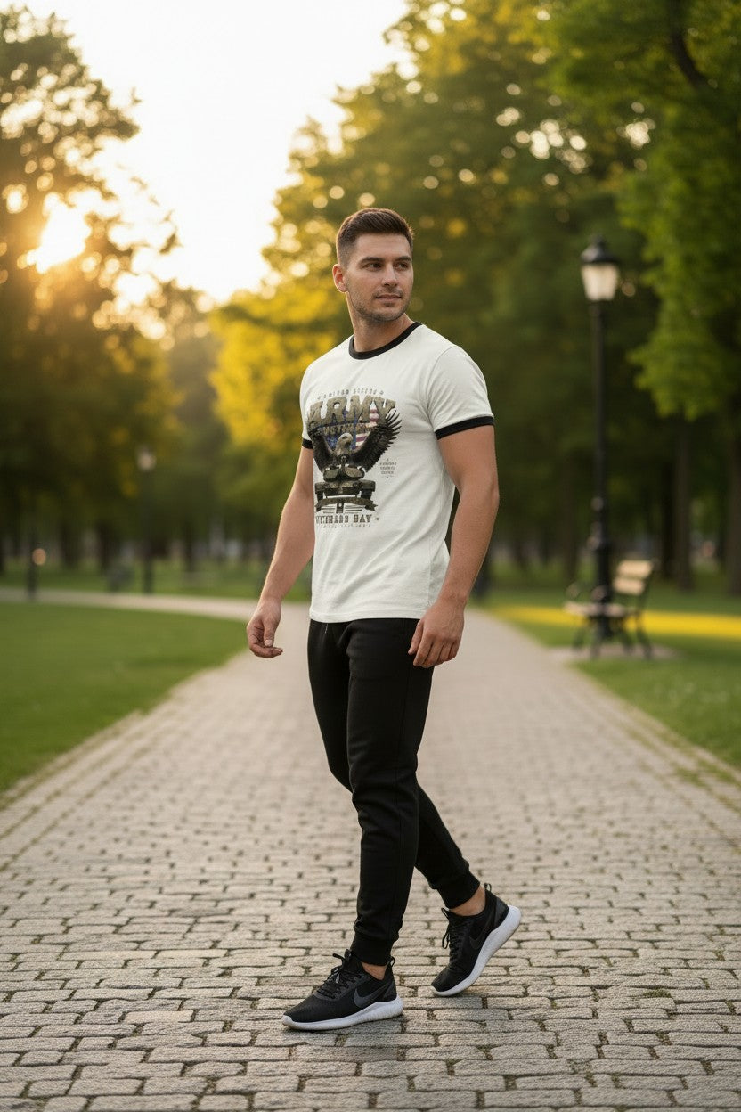 A man walking on a paved path in a park at sunset, wearing a white graphic t-shirt with black trim, black pants, and black sneakers.