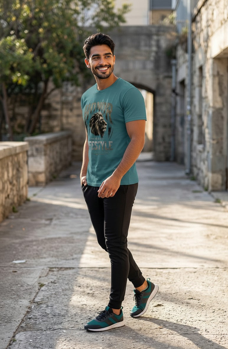 Man wearing a teal t-shirt with a graphic design, black pants, and green shoes standing on a stone path.