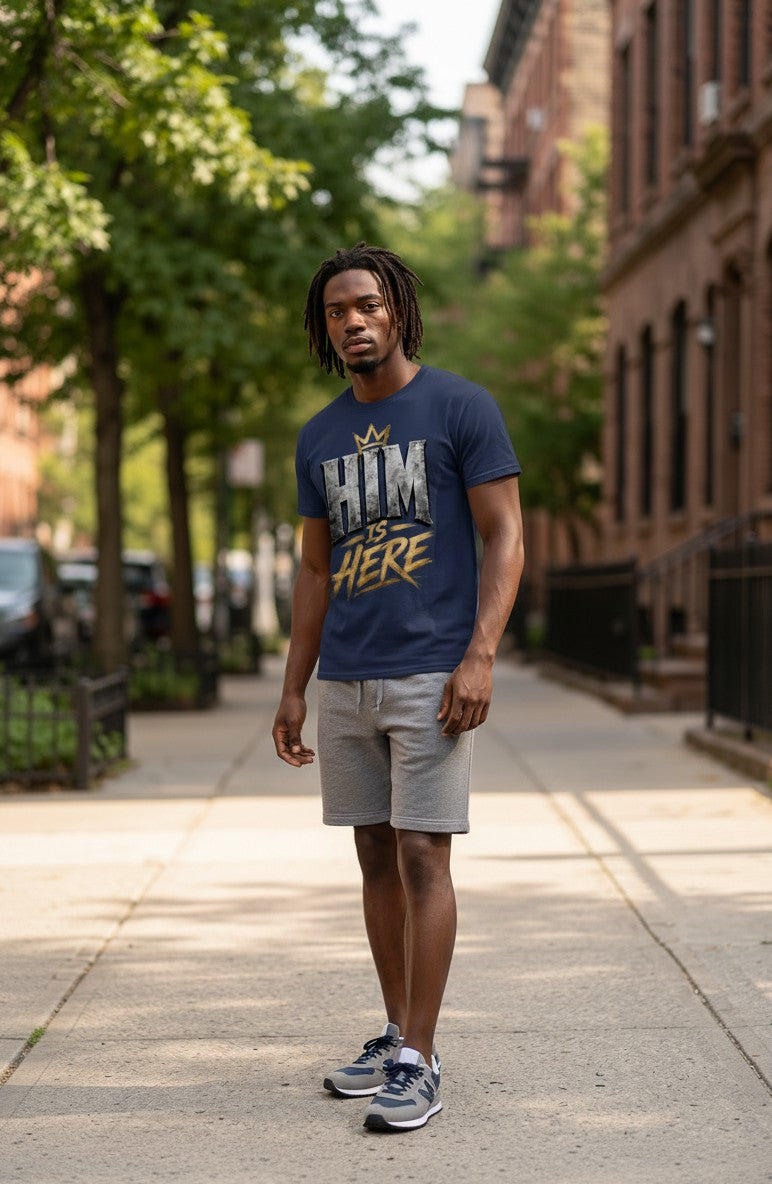 Man wearing a blue t-shirt with text standing on a sidewalk with trees and buildings in the background