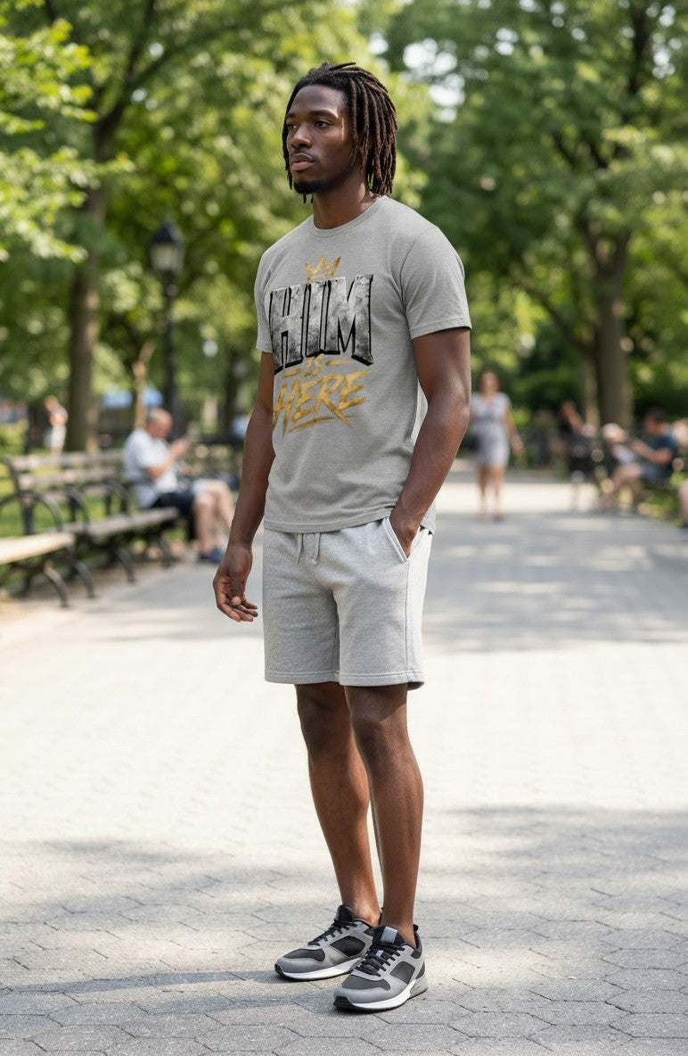 Man wearing a gray t-shirt and shorts standing on a paved path with trees in the background