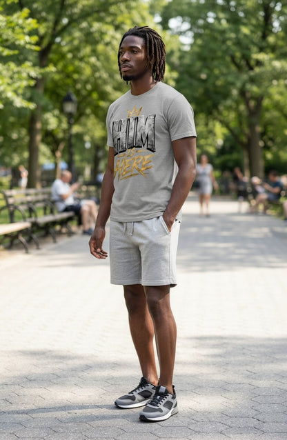 Man wearing a gray t-shirt and shorts standing on a paved path with trees in the background