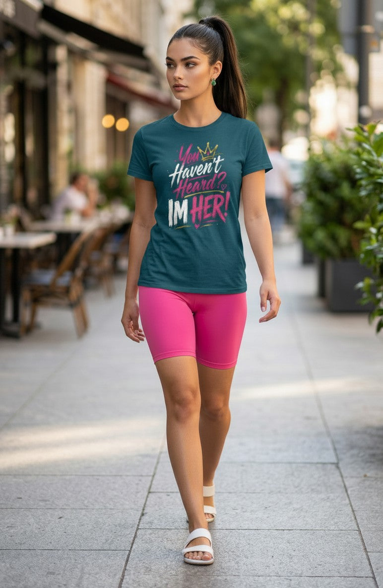 Woman walking outdoors wearing a teal t-shirt with a colorful graphic and pink shorts.
