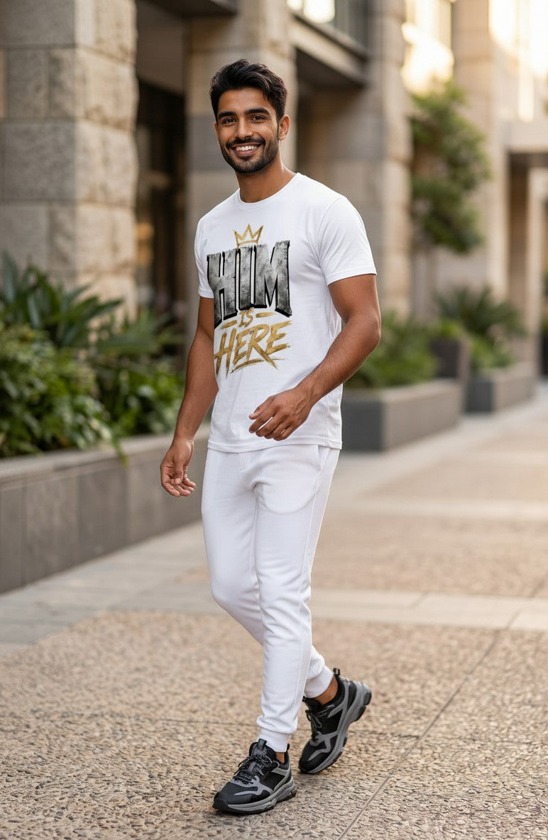 Man wearing a white t-shirt with 'HIM IS HERE' text walking on a sidewalk.