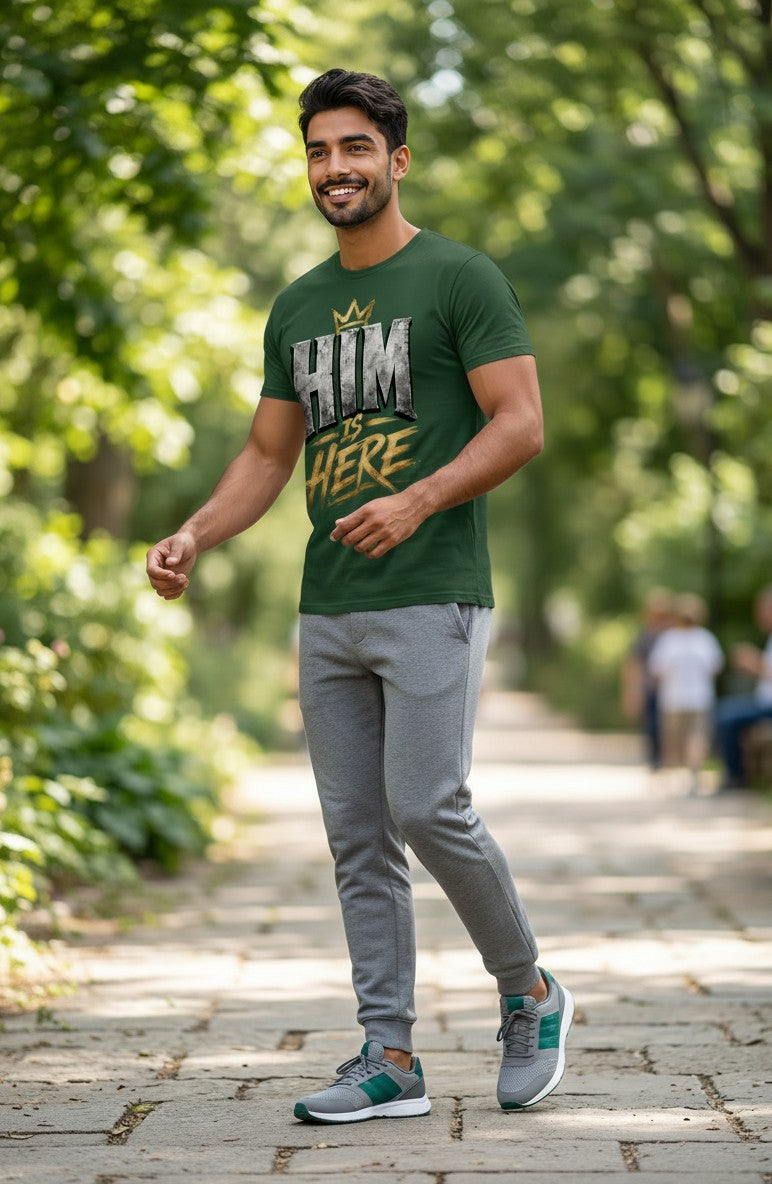 Man wearing a green t-shirt with text and gray pants walking on a path in a park.