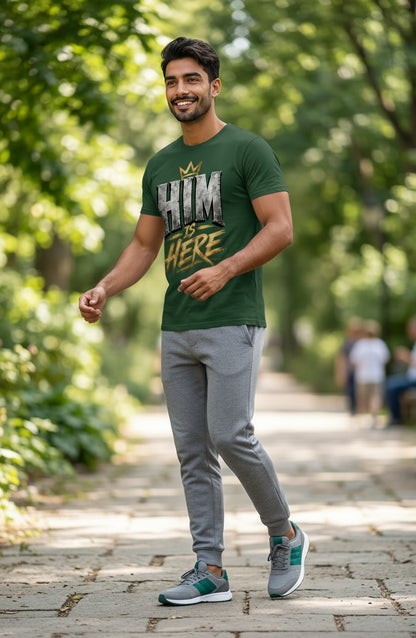 Man wearing a green t-shirt with text and gray pants walking on a path in a park.