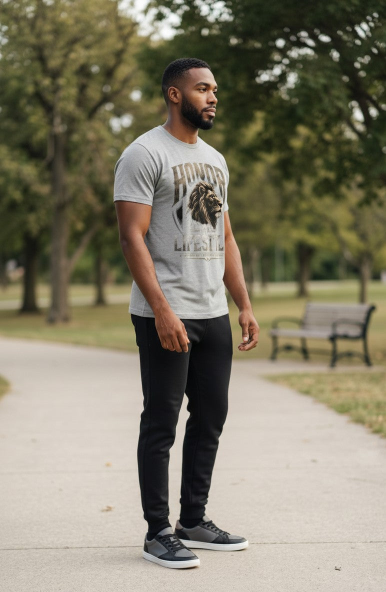 Man wearing a gray t-shirt with a lion graphic and text, standing on a path in a park.