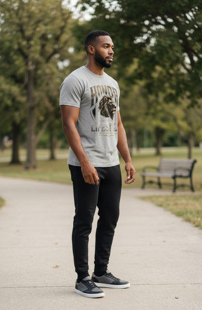 Man wearing a gray t-shirt with a lion graphic and text, standing on a path in a park.