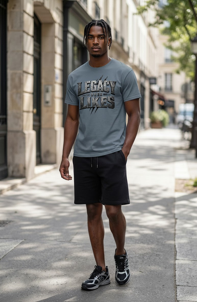 Man wearing a gray t-shirt with 'Legacy over Likes' text on a city street.