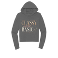 A dark gray cropped hoodie with a graphic text print reading 'CLASSY never BASIC' in rose gold and cream lettering, displayed on a solid white background.