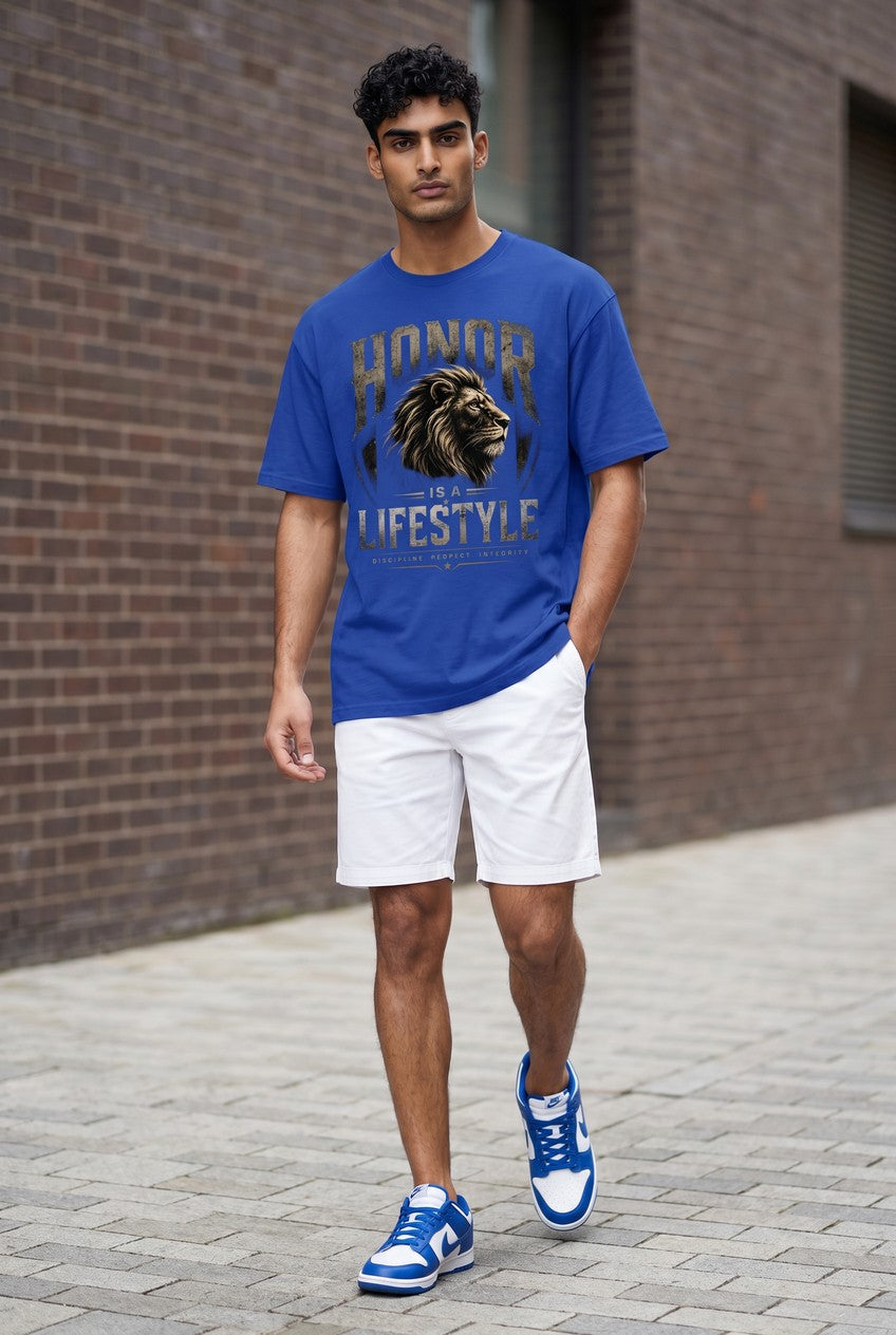Man wearing a blue t-shirt with a lion graphic and text, white shorts, and blue sneakers in front of a brick wall.