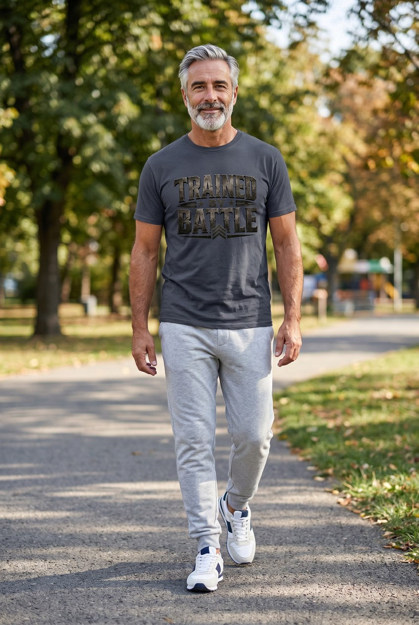 Man walking outdoors in a park wearing a gray t-shirt with text and light gray pants.