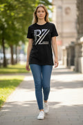 Woman wearing a black t-shirt with a logo and blue jeans walking on a sidewalk.