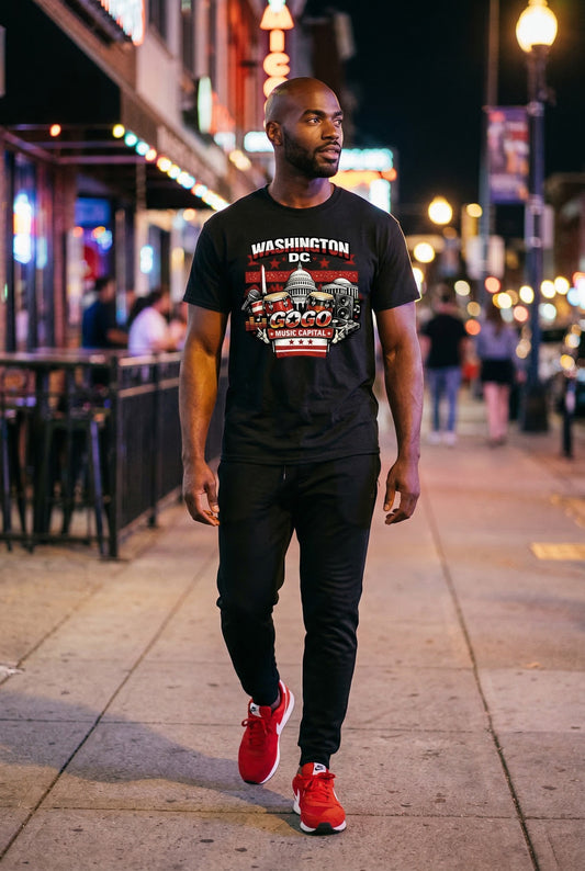 Man walking on a city street at night wearing a black t-shirt with a graphic design and red sneakers.