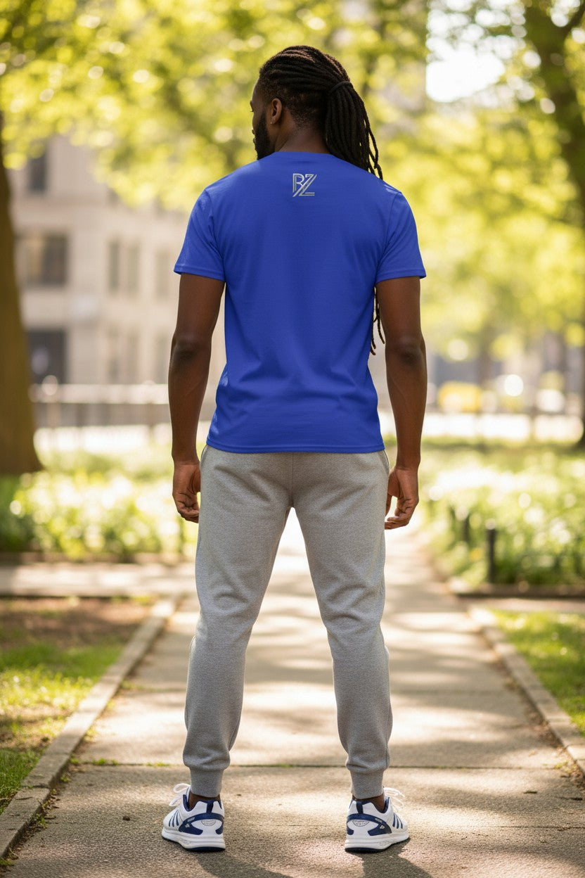 Person wearing a blue t-shirt with a logo on the back, standing on a path with greenery in the background.