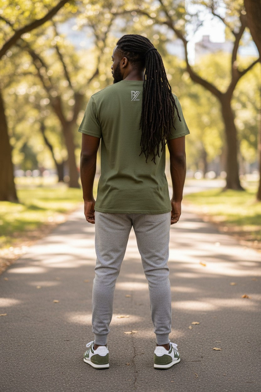 Man walking in a park wearing a green t-shirt and gray pants.