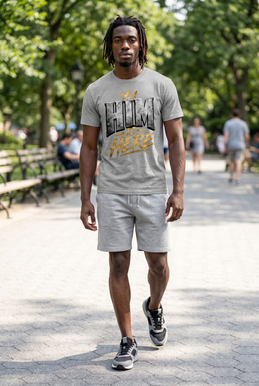 Man wearing a gray t-shirt with text and shorts in a park setting