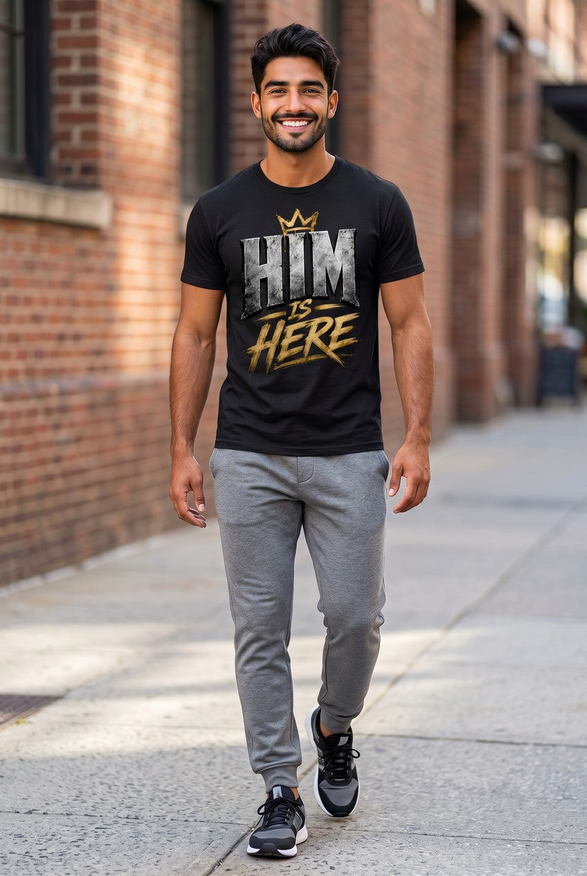 Man walking on a sidewalk wearing a black t-shirt with text and gray pants.