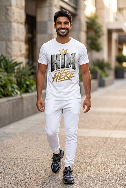Man wearing a white t-shirt with 'HIM IS HERE' text walking on a sidewalk.