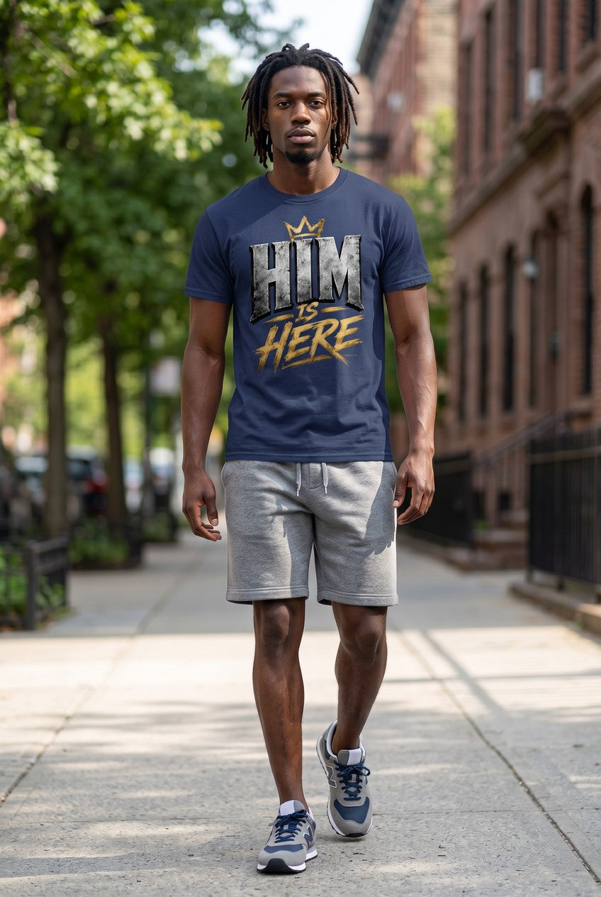 Man wearing a blue t-shirt with 'HIM IS HERE' text on a city street.