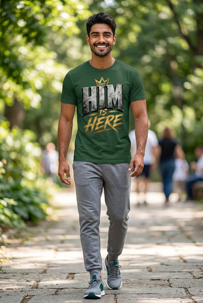 Man walking outdoors wearing a green t-shirt with 'HIM IS HERE' text