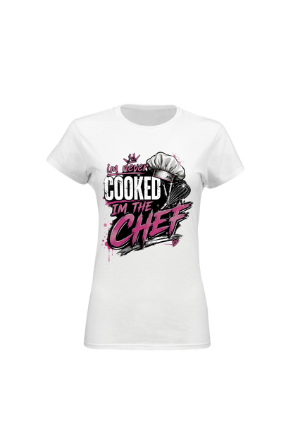 A white short-sleeve crewneck t-shirt with a graphic print on the front. The graphic features a chef's hat and the text 'Las never COOKED I'M THE CHEF' in black and pink lettering.