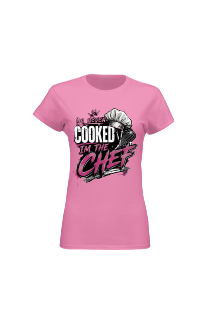 A pink short-sleeve crewneck t-shirt with a graphic on the front that reads 'I've never COOKED I'M THE CHEF' in stylized white, black, and pink lettering, accompanied by a chef's hat illustration.