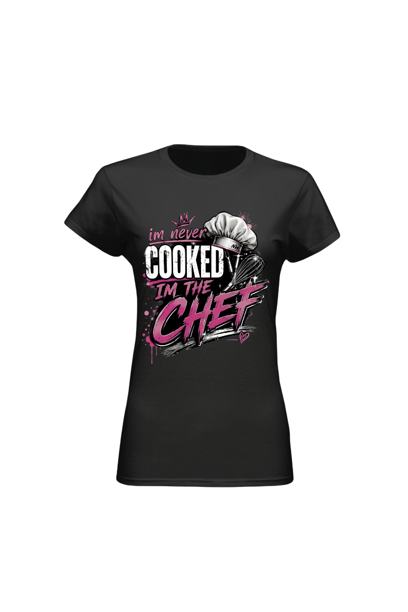 A black short-sleeve crewneck t-shirt with a graphic on the front that reads 'I'm never COOKED I'm THE CHEF' in white and pink lettering, featuring a chef's hat illustration.