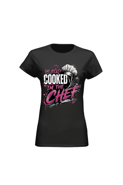A black short-sleeve crewneck t-shirt with a graphic on the front that reads 'I'm never COOKED I'm THE CHEF' in white and pink lettering, featuring a chef's hat illustration.