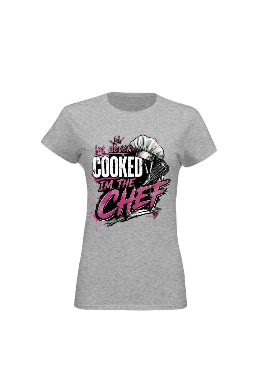 A women's heather gray short-sleeve t-shirt with a graphic on the front that reads 'I've never COOKED I'M THE CHEF' in white and pink lettering, accompanied by a chef's hat illustration.