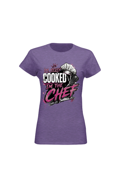 A women's short-sleeve crewneck t-shirt in heather purple, featuring a graphic print on the front with the text 'I DO NEVER COOKED I'M THE CHEF' in white and pink lettering alongside a chef's hat illustration.
