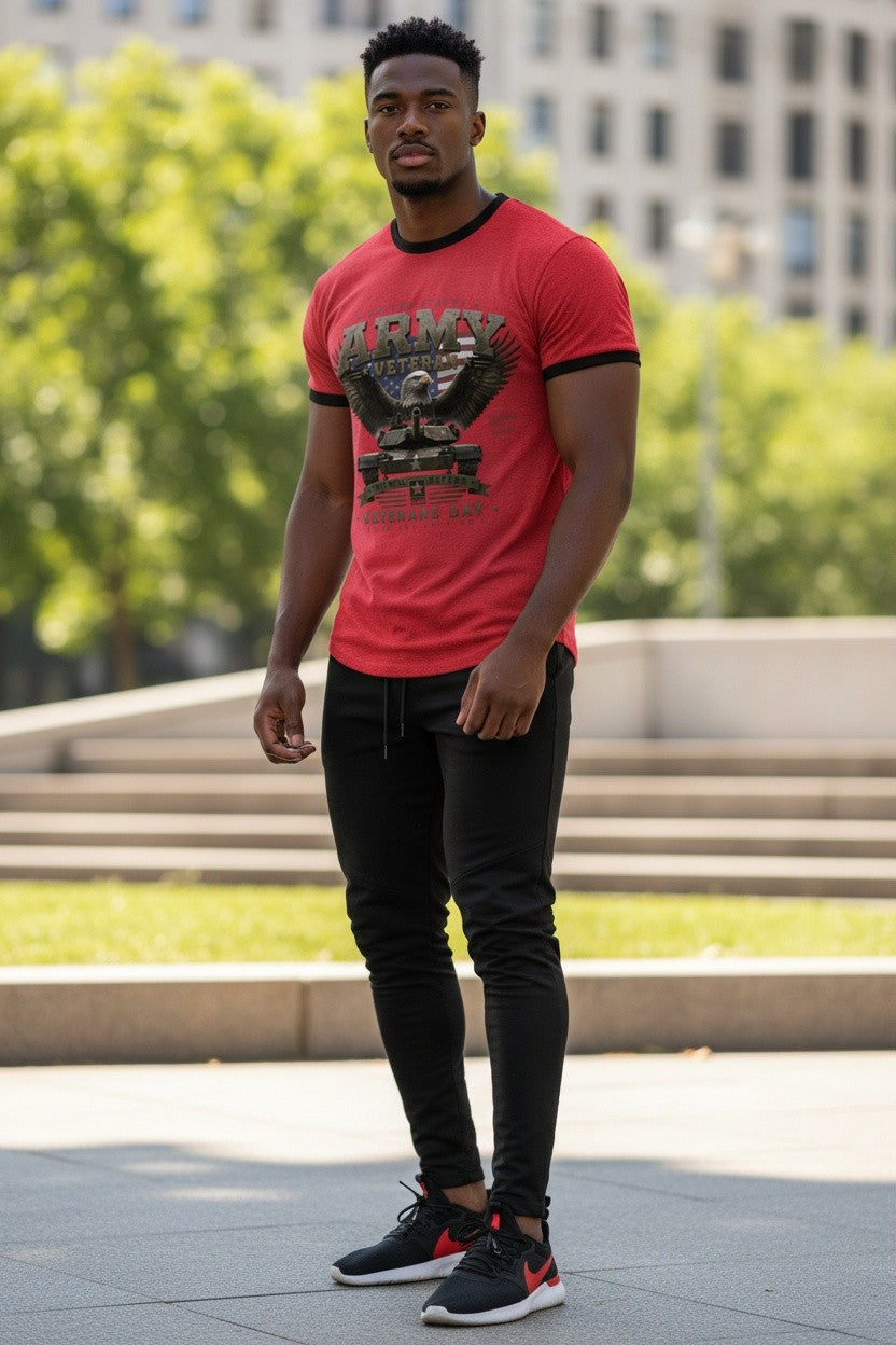 A man standing outdoors in a park-like setting wearing a red short-sleeve t-shirt with a black graphic print, black pants, and black sneakers with red accents.
