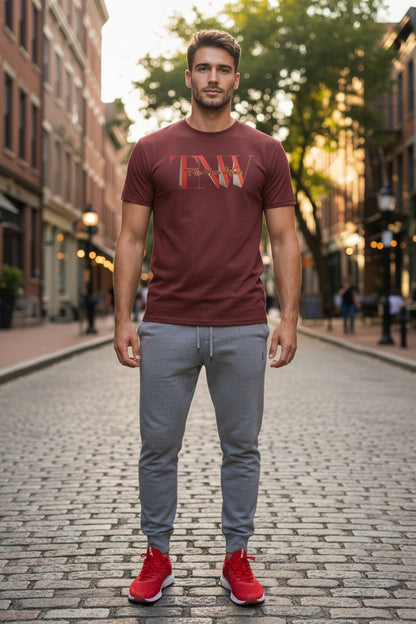 Man wearing a maroon t-shirt with 'TNW' logo, gray pants, and red shoes on a cobblestone street.