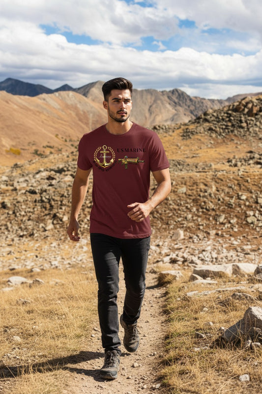 Man walking on a trail in a mountainous landscape wearing a maroon t-shirt with a logo.