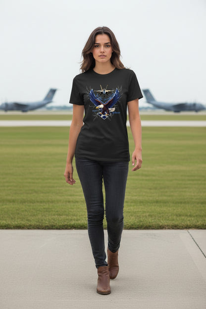 Woman wearing a black t-shirt with an eagle design on a grassy area with airplanes in the background