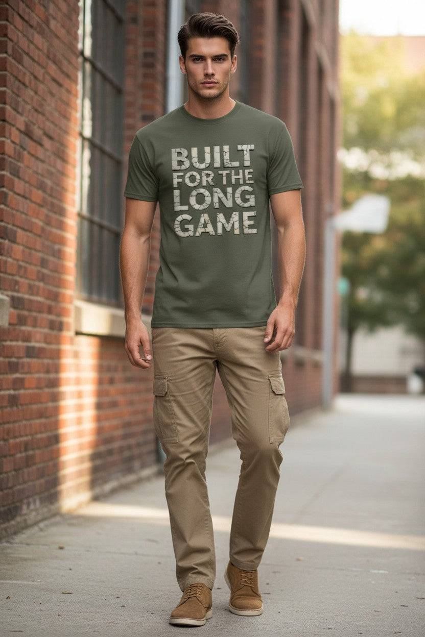 Man wearing a green t-shirt with 'Built for the Long Game' text, standing on a sidewalk.