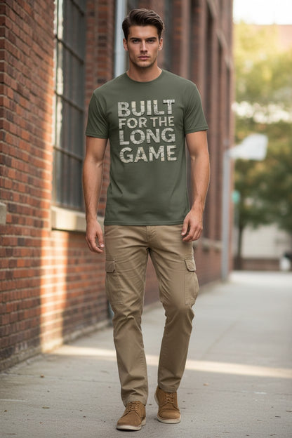 Man wearing a green t-shirt with 'Built for the Long Game' text, standing on a sidewalk.